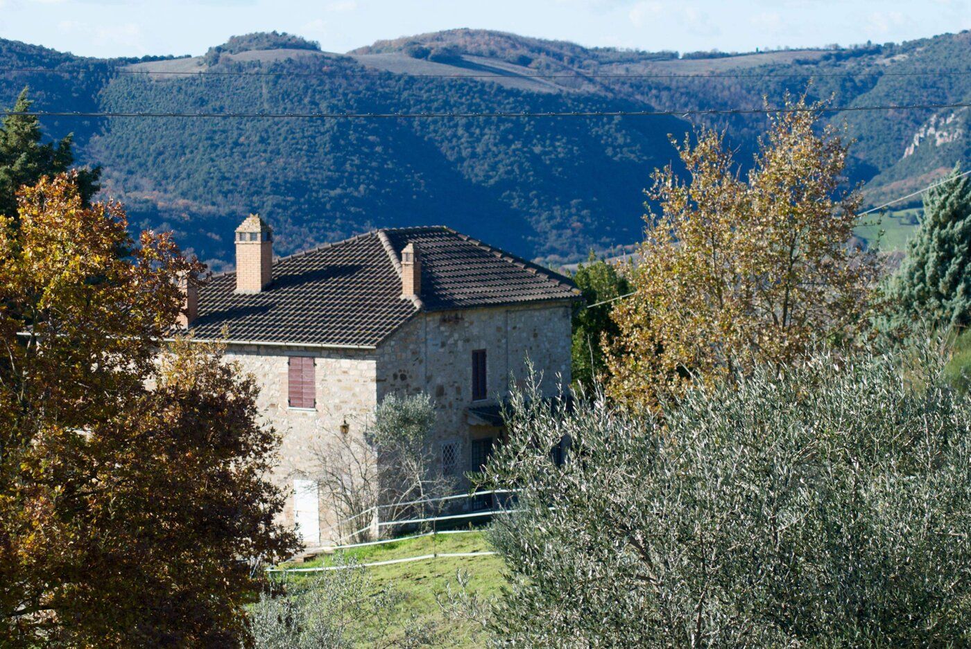 Casolare in pietra tra gli alberi, con le colline sullo sfondo